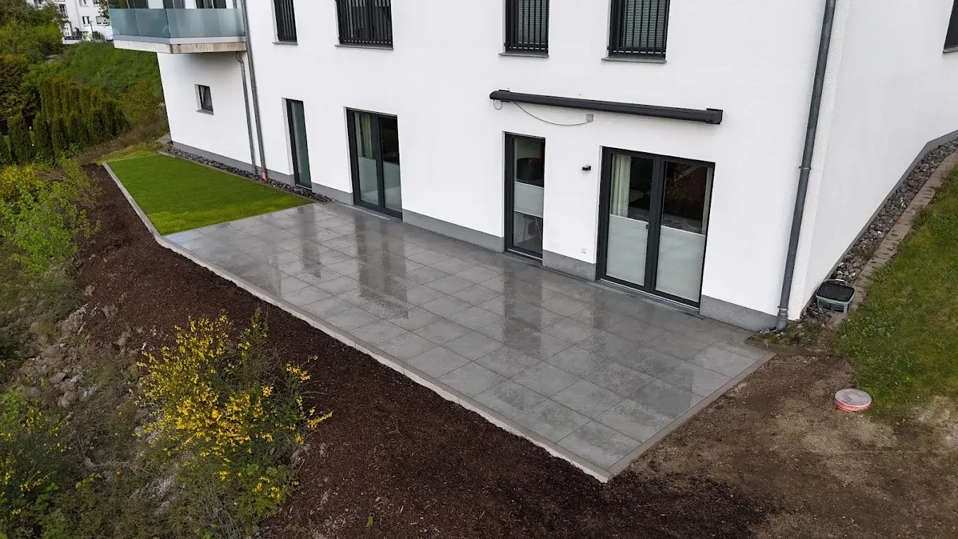 Neue Terrasse mit grauen Platten an der Hauswand